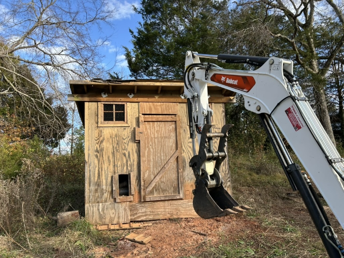 Excavator demolishing wooden shed structure
