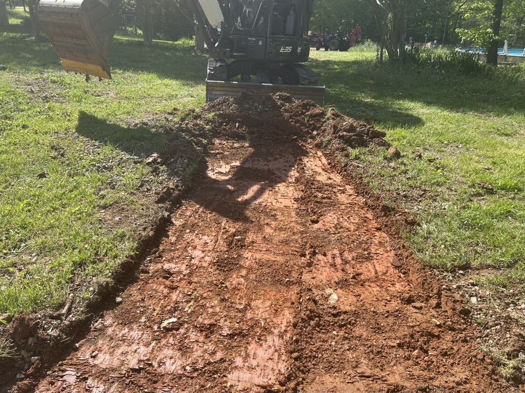 Mini excavator digging trench grassy yard